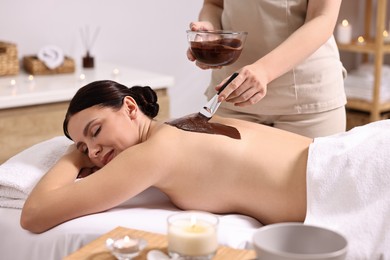 Photo of Chocolate body wrap. Spa worker applying mask onto woman's back in salon, closeup