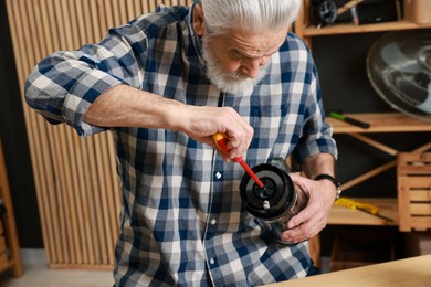 Photo of Relaxing hobby. Senior man repairing blender with screwdriver in workshop