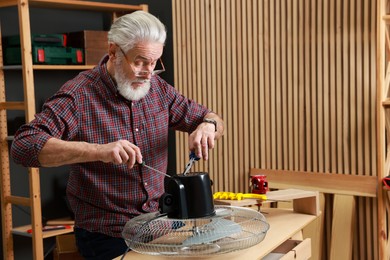 Photo of Relaxing hobby. Senior man repairing fan in workshop