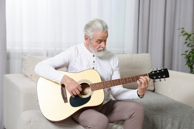 Photo of Relaxing hobby. Senior man playing guitar on sofa at home