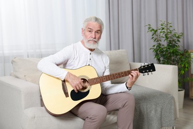 Photo of Relaxing hobby. Senior man playing guitar on sofa at home