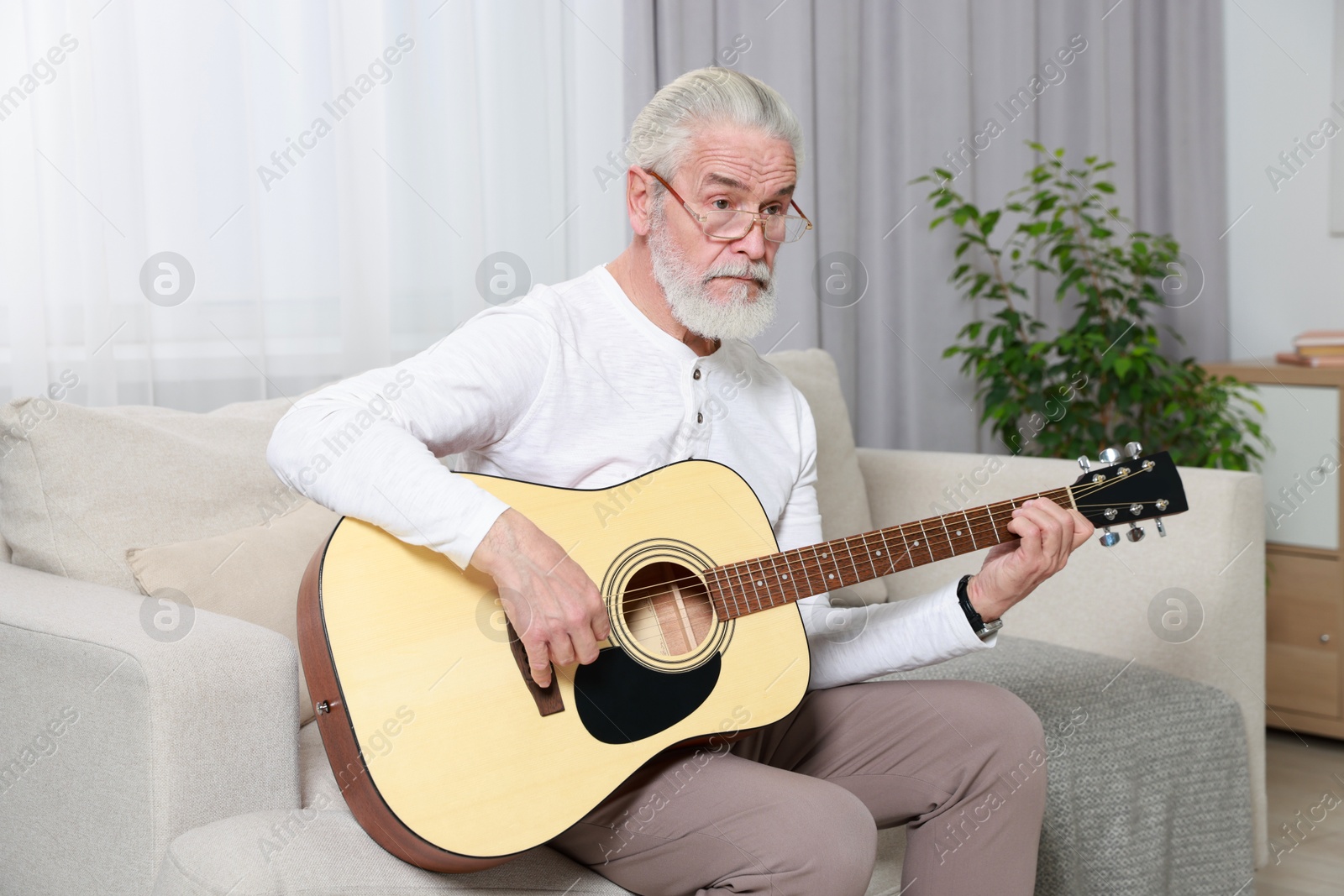 Photo of Relaxing hobby. Senior man playing guitar on sofa at home