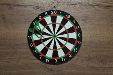 Photo of Dart board with green arrows on wooden background, top view