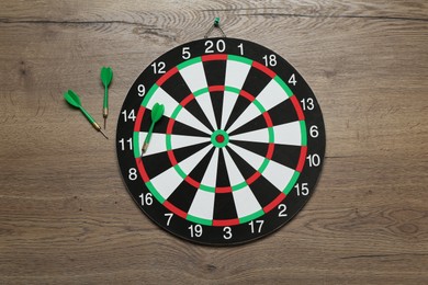 Photo of Dart board and green arrows on wooden background, flat lay