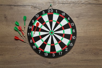 Photo of Dart board and colorful arrows on wooden background, flat lay