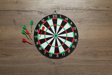 Photo of Dart board and colorful arrows on wooden background, flat lay