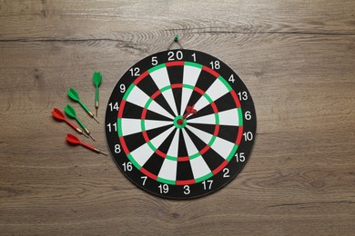 Photo of Dart board and colorful arrows on wooden background, flat lay