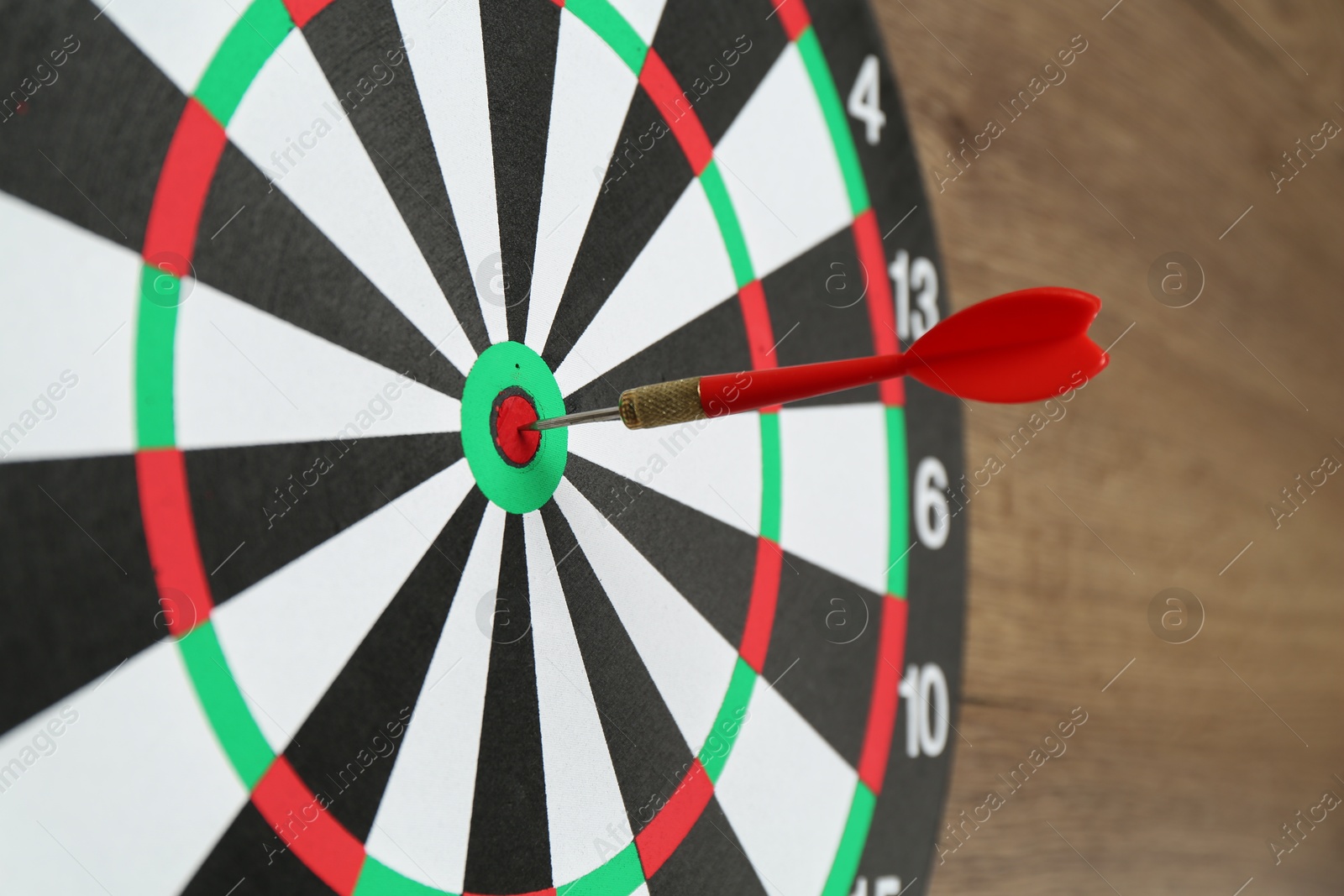 Photo of Dart board and red arrow on wooden background, closeup