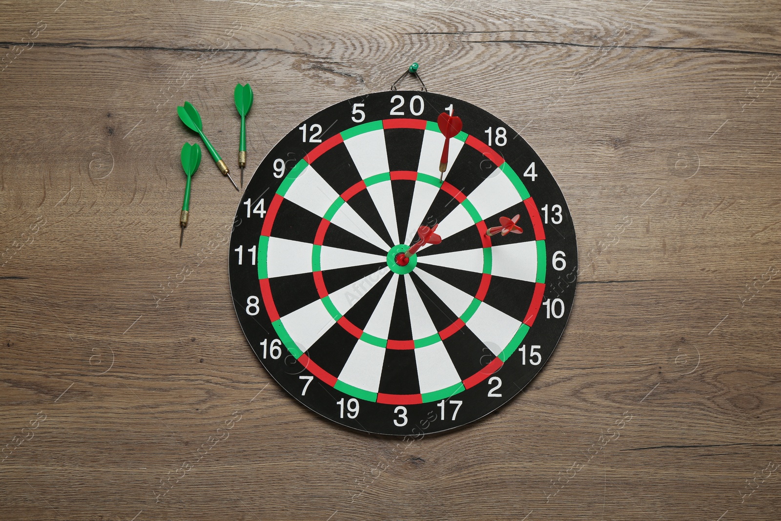 Photo of Dart board and green arrows on wooden background, flat lay