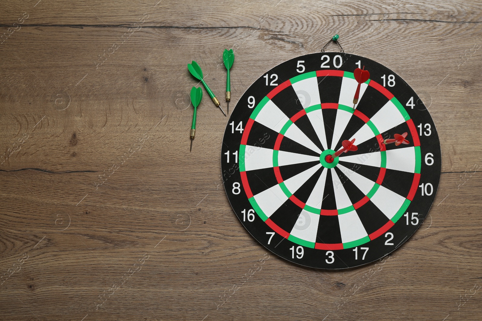 Photo of Dart board and green arrows on wooden background, flat lay. Space for text