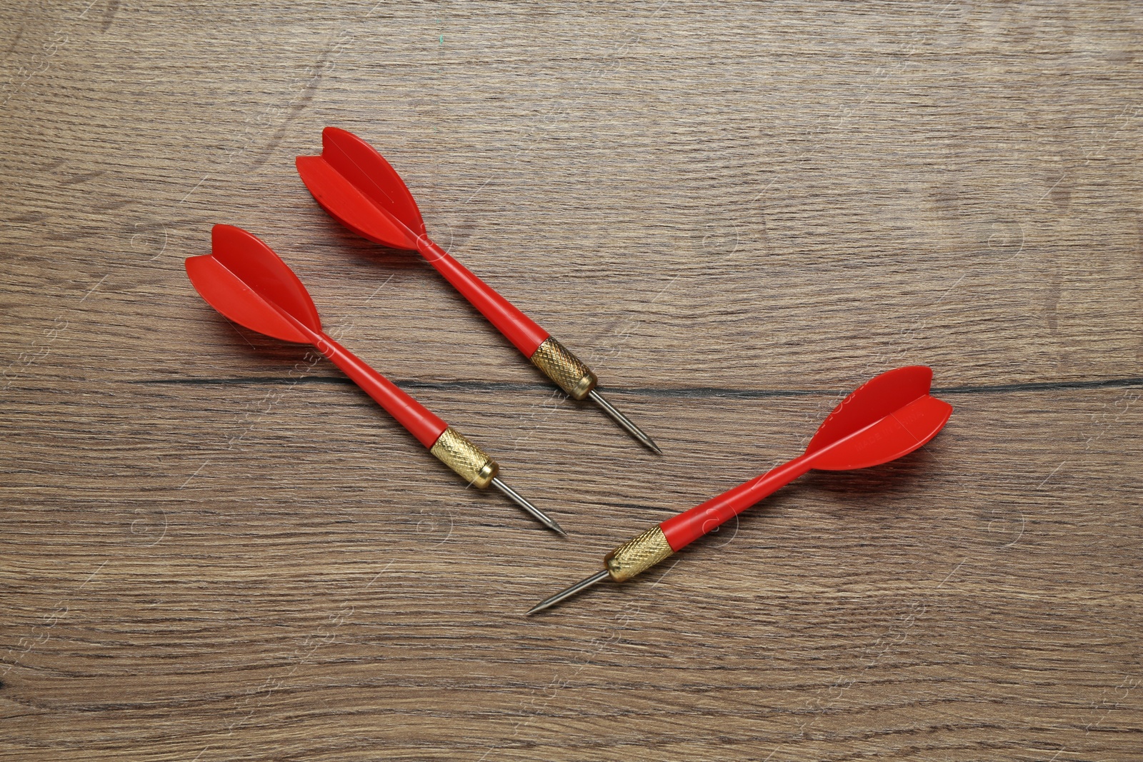 Photo of Red dart arrows on wooden table, flat lay