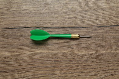 Photo of One green dart arrow on wooden table, top view