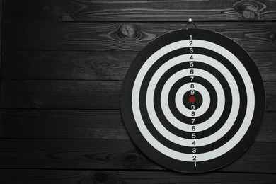 Photo of One dart board hanging on black wooden background. Space for text