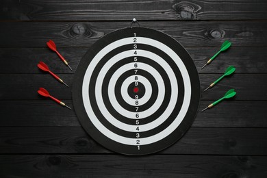 Photo of Dart board and colorful arrows on black wooden background, flat lay