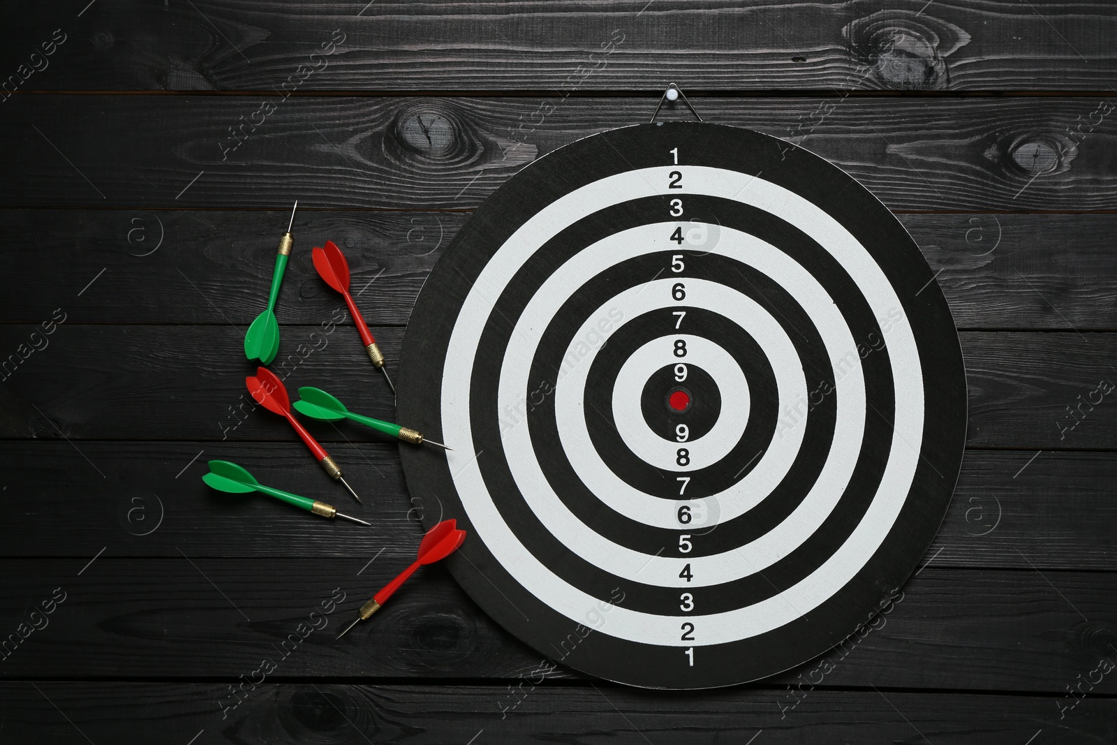 Photo of Dart board and colorful arrows on black wooden background, flat lay