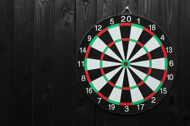 Photo of One dart board hanging on black wooden background. Space for text