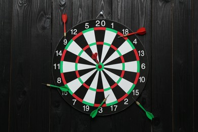 Photo of Dart board and colorful arrows on black wooden background, flat lay