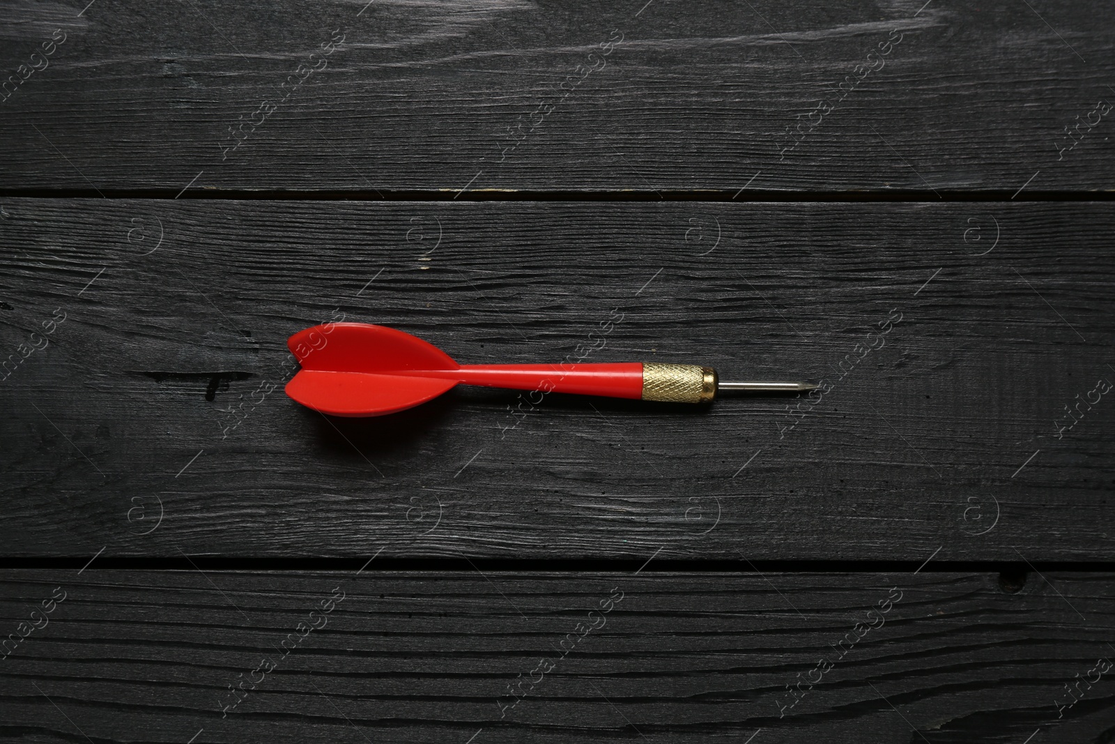 Photo of One red dart arrow on black wooden table, top view