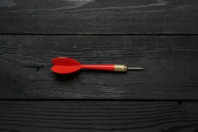 Photo of One red dart arrow on black wooden table, top view