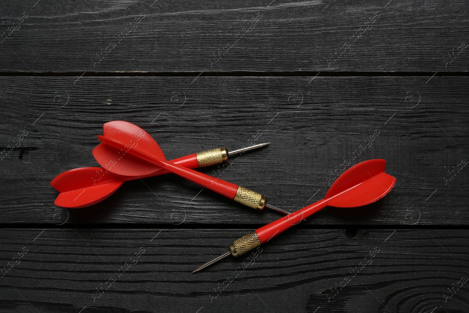 Photo of Red dart arrows on black wooden table, flat lay