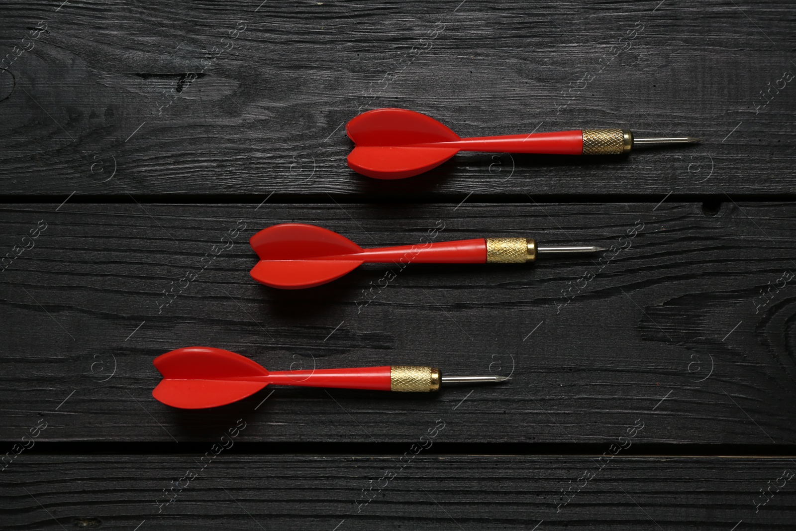 Photo of Red dart arrows on black wooden table, flat lay