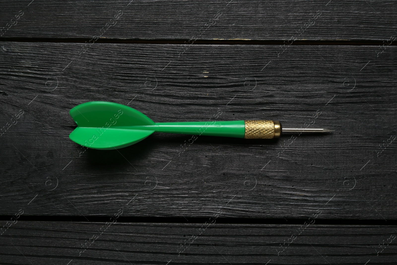 Photo of One green dart arrow on black wooden table, top view