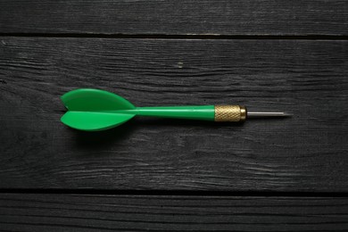 Photo of One green dart arrow on black wooden table, top view