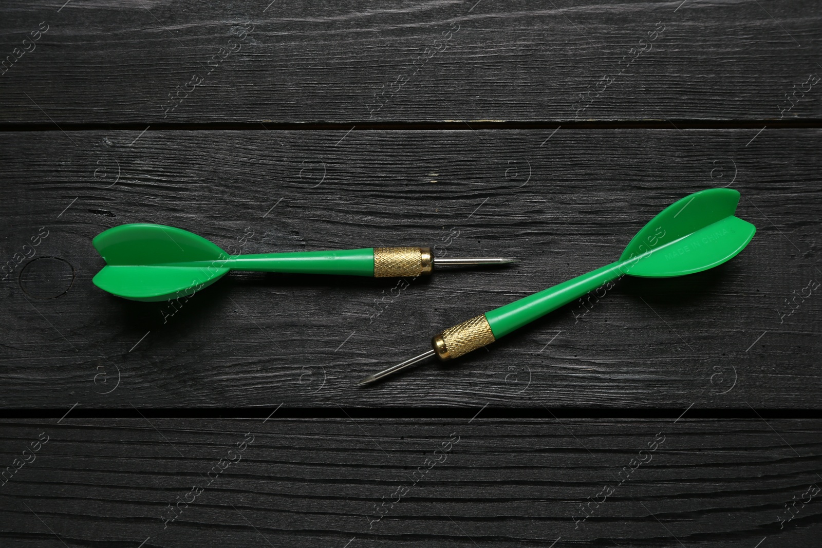 Photo of Green dart arrows on black wooden table, flat lay