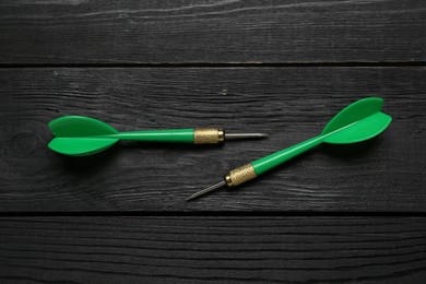 Photo of Green dart arrows on black wooden table, flat lay