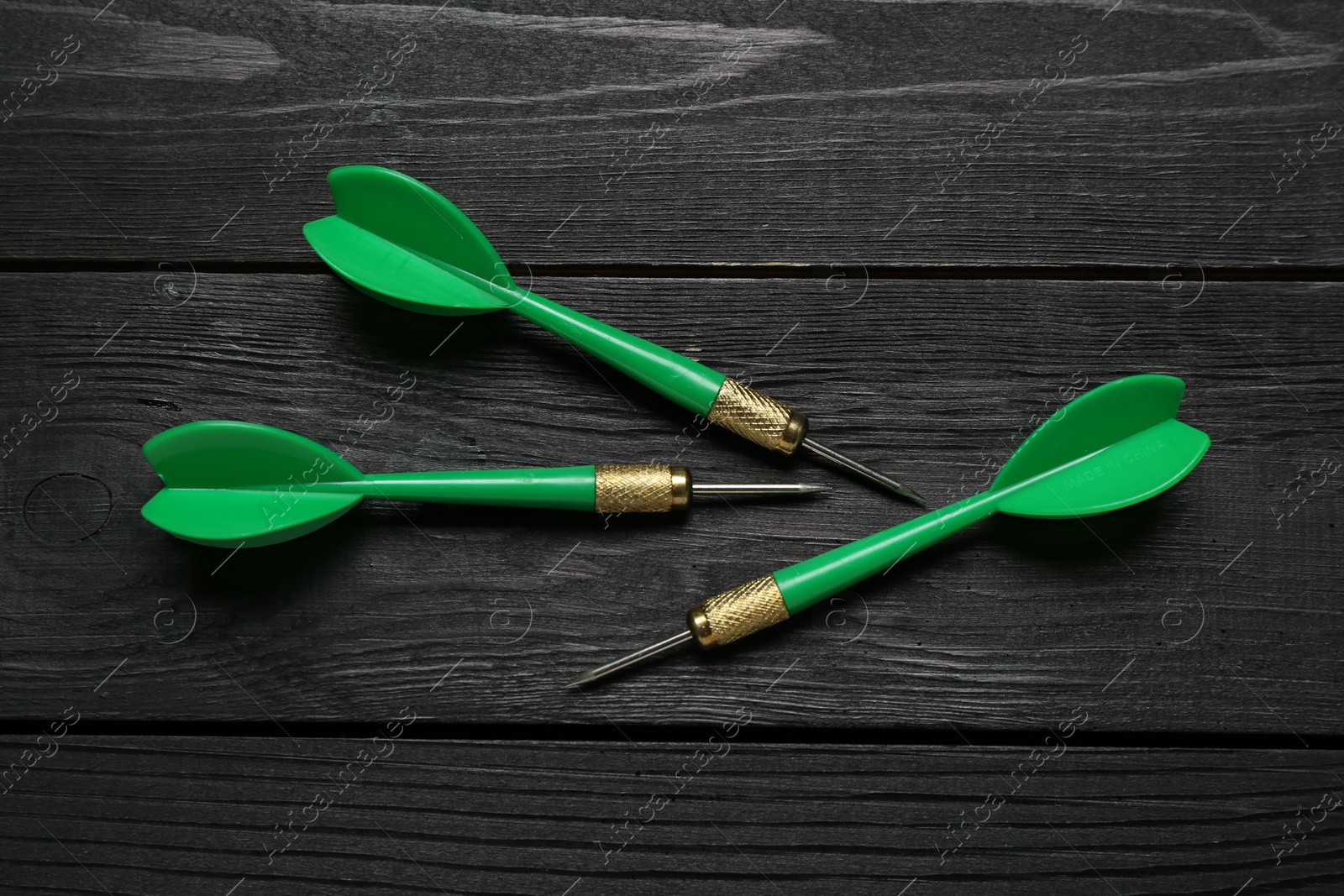 Photo of Green dart arrows on black wooden table, flat lay