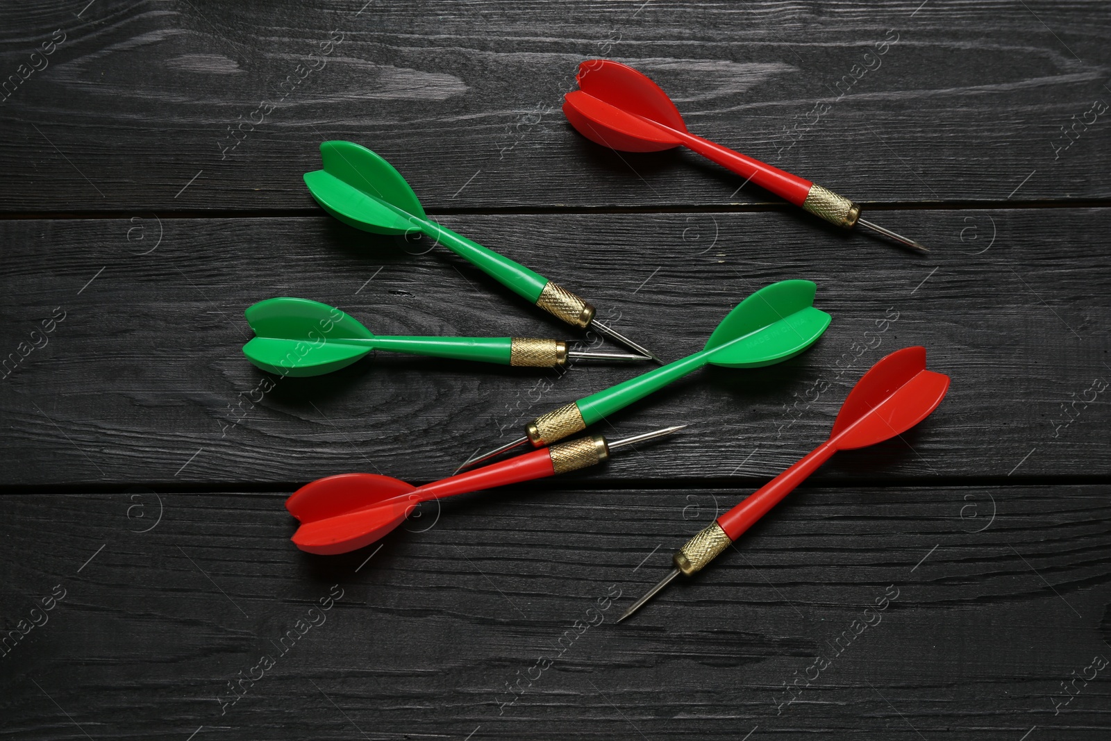 Photo of Colorful dart arrows on black wooden table, flat lay