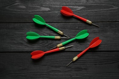 Photo of Colorful dart arrows on black wooden table, flat lay