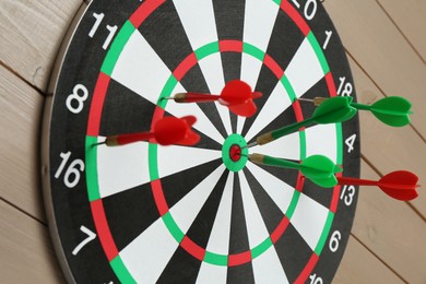 Photo of Dart board with colorful arrows on wooden background, closeup