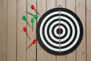 Photo of Dart board and colorful arrows on wooden background, flat lay. Space for text