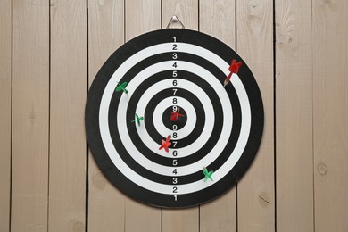 Photo of Dart board with colorful arrows hanging on wooden background