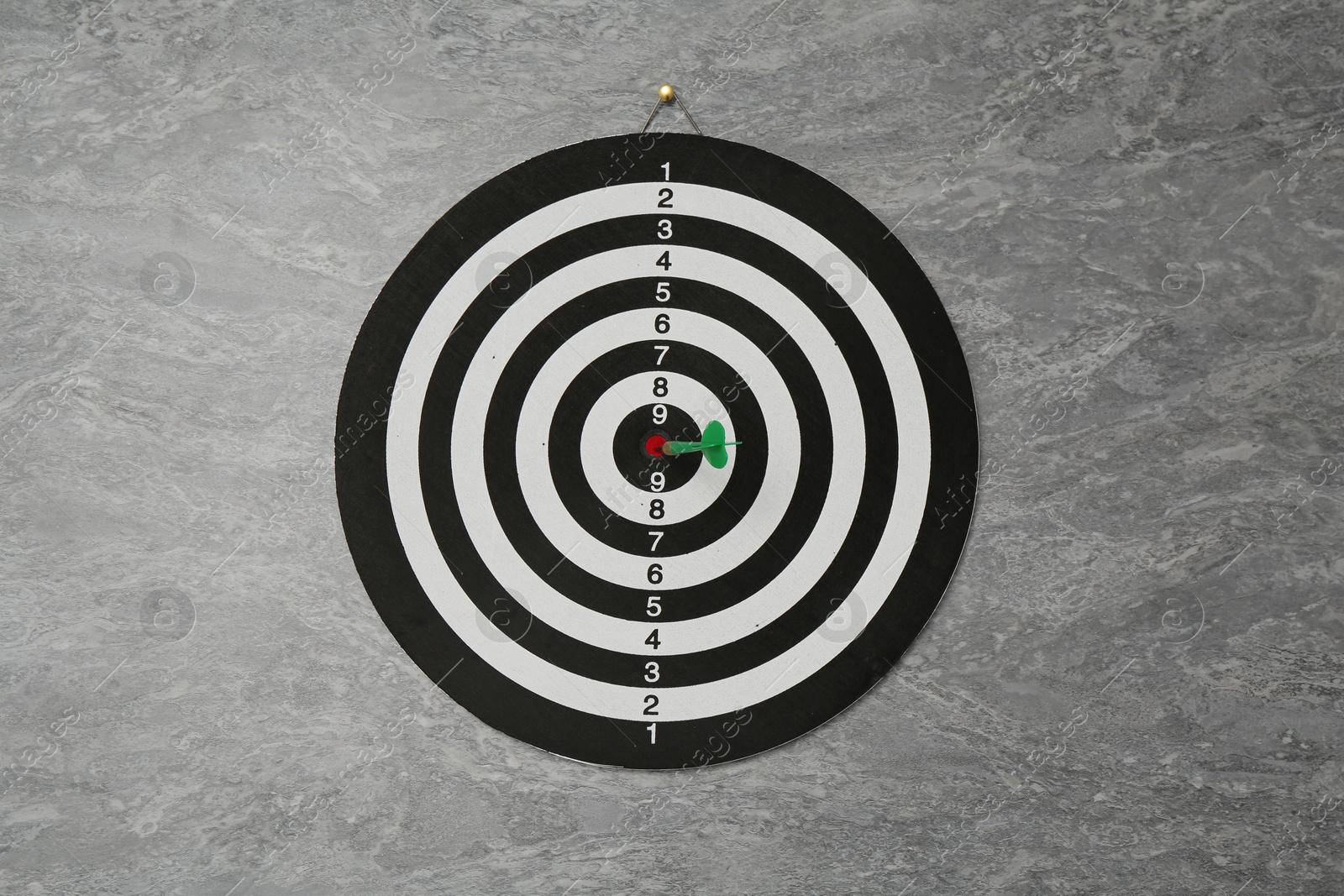 Photo of Dart board with green arrow hanging on grey marble wall