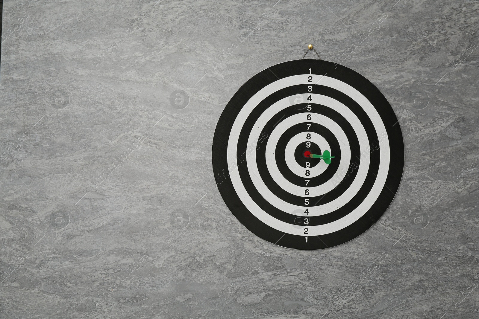 Photo of Dart board with green arrow hanging on grey marble wall, space for text