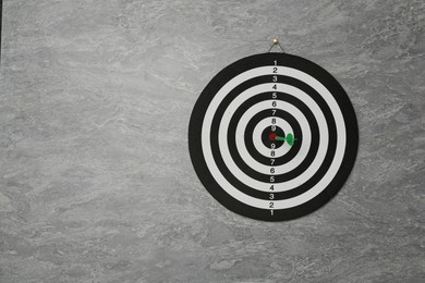 Photo of Dart board with green arrow hanging on grey marble wall, space for text