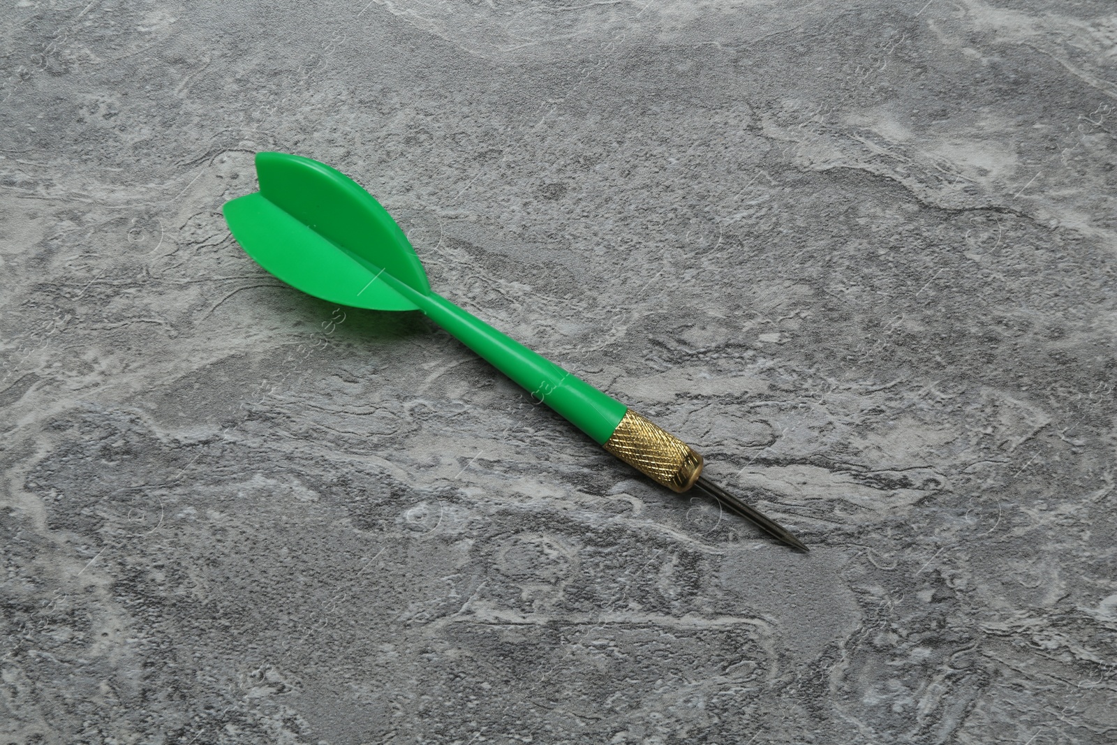 Photo of One green dart arrow on grey textured table, top view