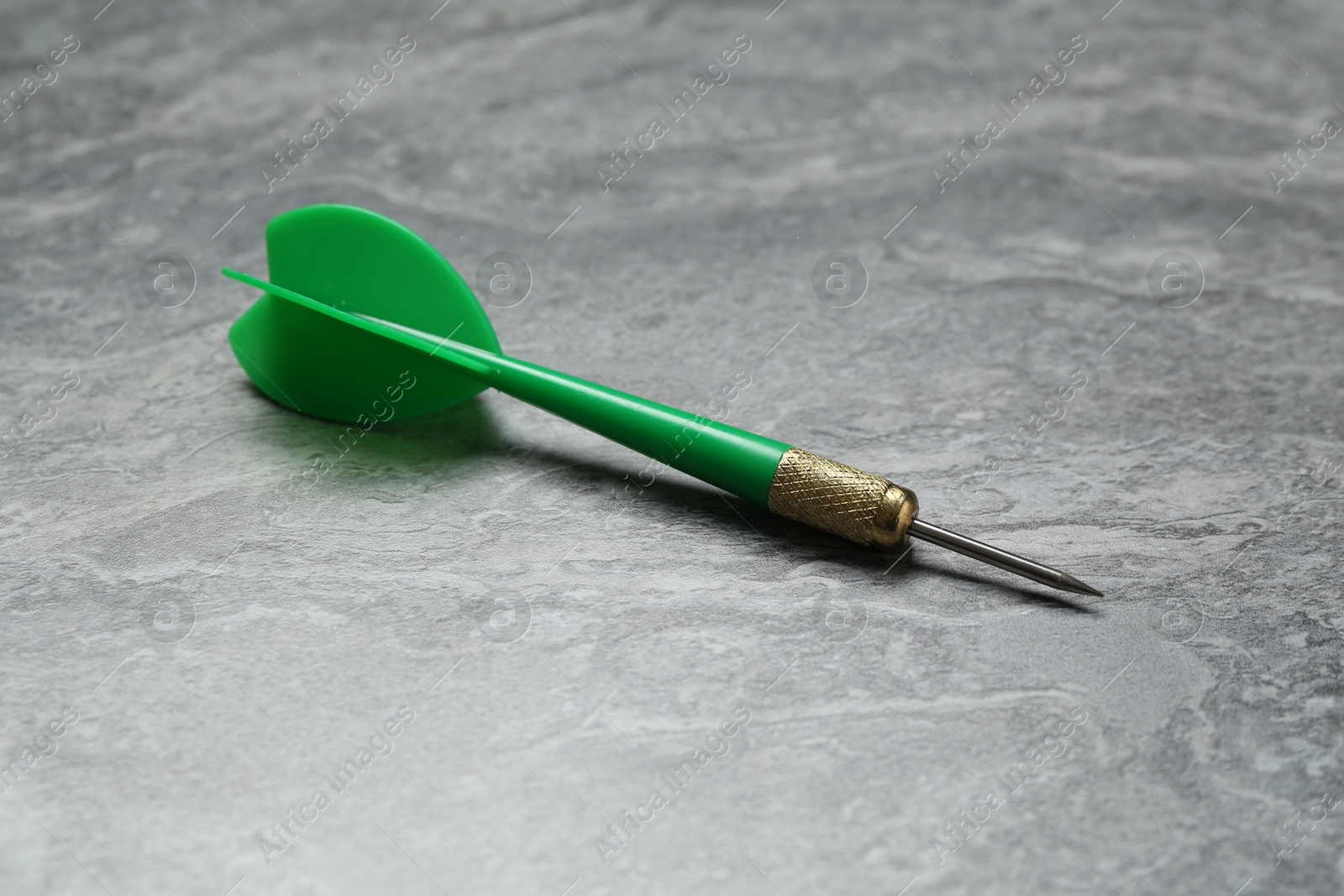 Photo of One green dart arrow on grey textured table, closeup