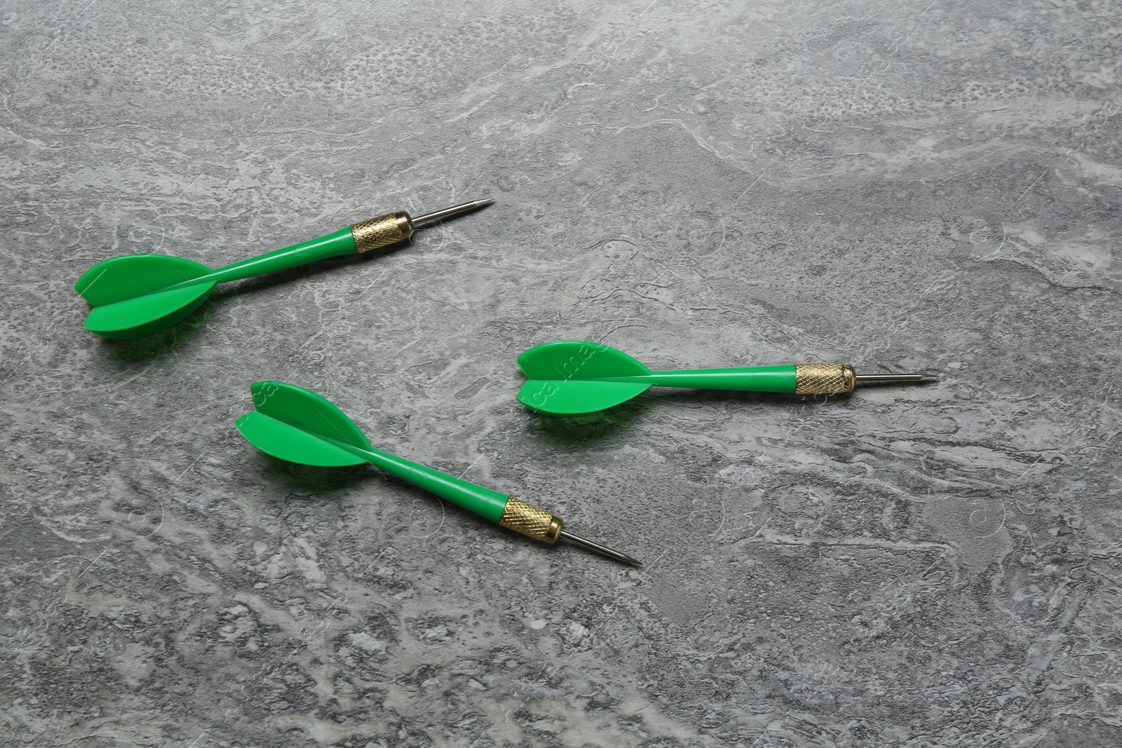 Photo of Green dart arrows on grey textured table, flat lay