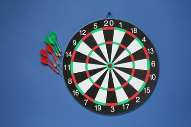 Photo of Dart board and colorful arrows on blue background, flat lay