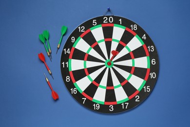 Photo of Dart board and colorful arrows on blue background, flat lay