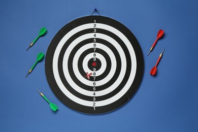 Photo of Dart board and colorful arrows on blue background, flat lay