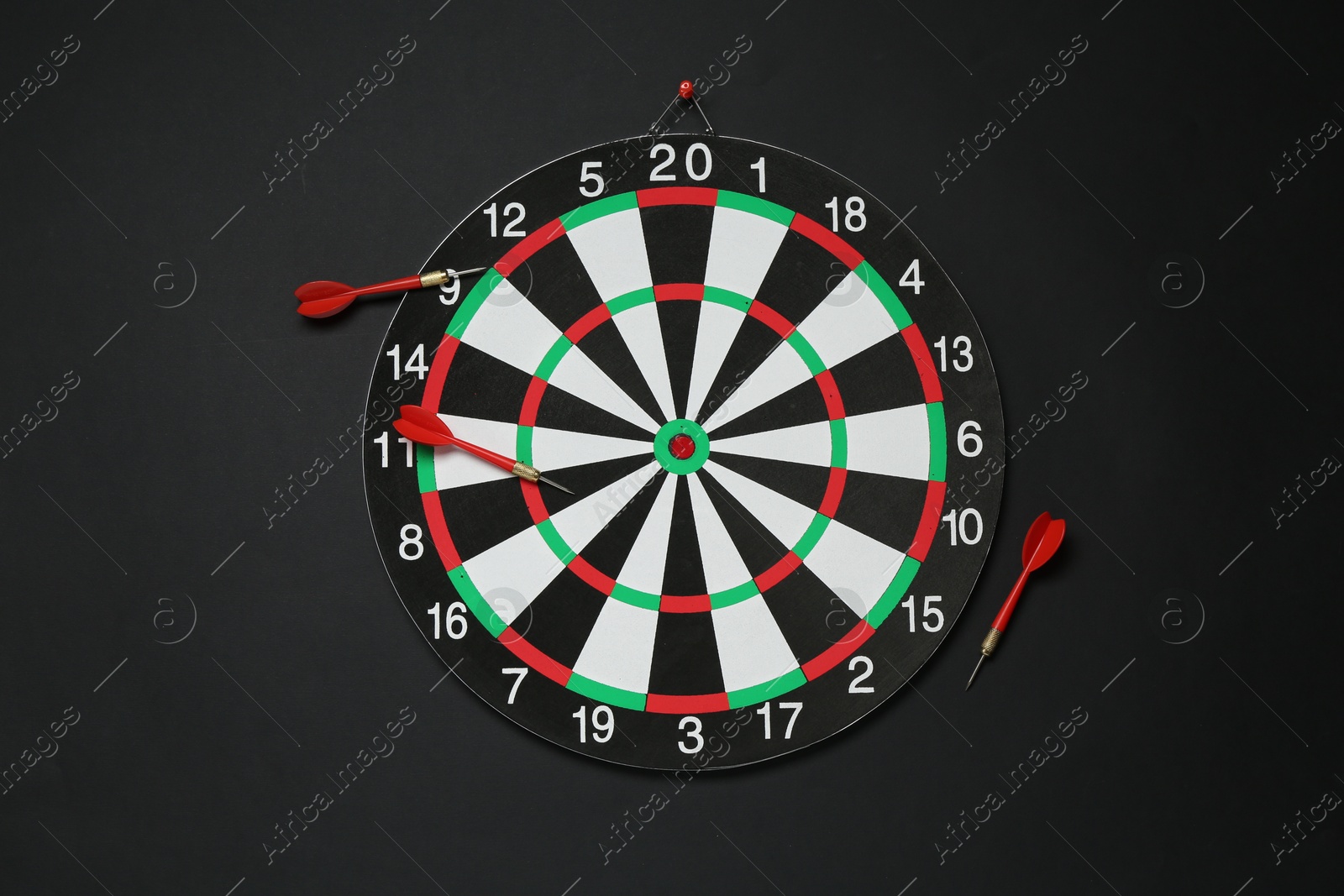 Photo of Dart board and red arrows on black background, flat lay