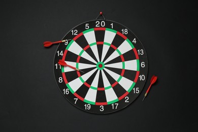 Photo of Dart board and red arrows on black background, flat lay