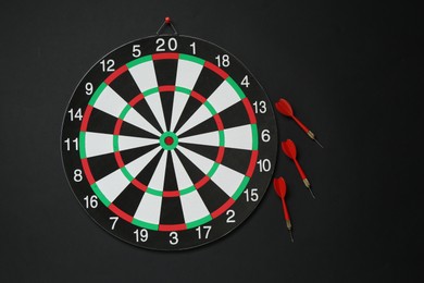 Photo of Dart board and red arrows on black background, flat lay