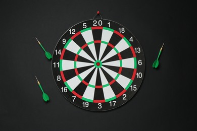 Photo of Dart board and green arrows on black background, flat lay