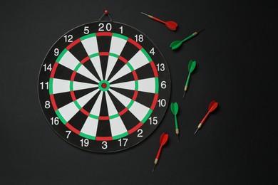 Photo of Dart board and colorful arrows on black background, flat lay