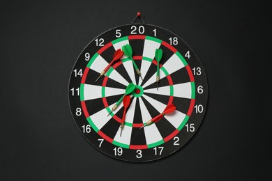 Photo of Dart board and colorful arrows on black background, top view